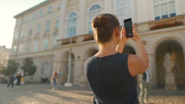 Woman stands on an old street and takes a photo or video on a smartphone at sunset