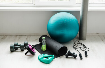 Group of different exercising equipment on white home gym floor. Fitness ball, round foam roller, resistance exercise latex band, jumping rope, dumbbells,  yoga mat. Fit lifestyle concept.