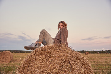 Tinted portrait of a young girl in a warm sweater, sitting by a haystack.