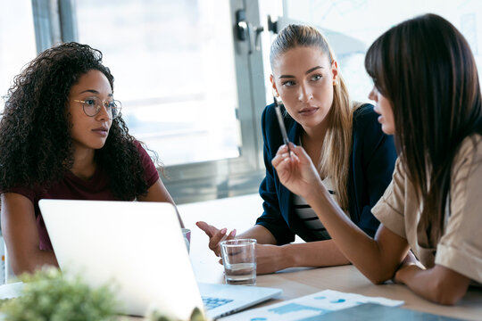 Three modern businesswomen talking and reviewing the latest work done on the computer in a joint workspace