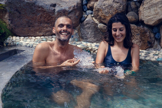 Young man and woman having recreational bath in the water filled with ice cubes. Multiethnic couple getting cryo therapy outdoors during summer