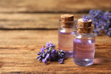 Bottles of essential oil and lavender flowers on wooden table. Space for text