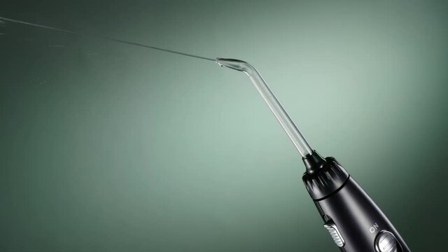 Black oral irrigator streams on green background. Working water flosser ready to clean teeth. Dental care, healthcare technology. 4k 120 fps
