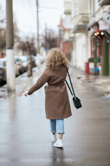 A portrait from the back of a curly-haired young woman who walks the streets of the city.