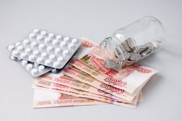 A glass jar with coins lies on five-thousand-dollar bills and medicines, the concept of medical expenses