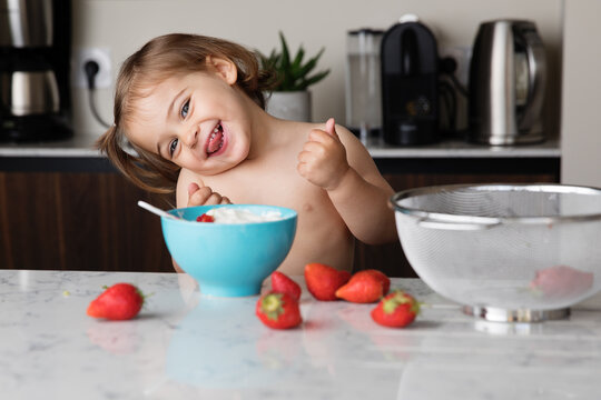 Happy Toddler Girl In Kitchen Eating Strawberries And Cream