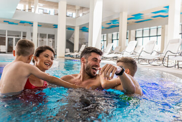 Smiling family of four having fun and relaxing in indoor swimming pool at hotel resort.