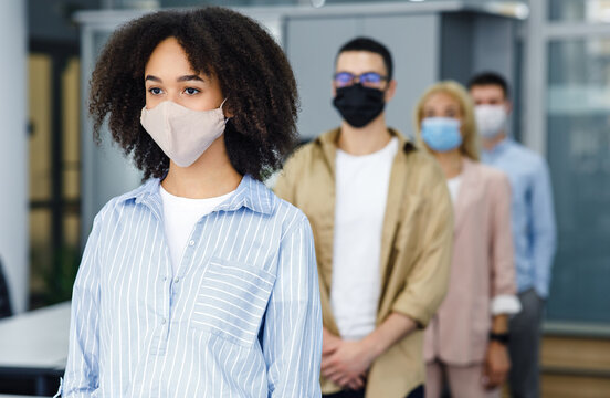 New normal and temperature check before work. Millennial multiracial employees in protective masks stand in line with social distancing at office in morning
