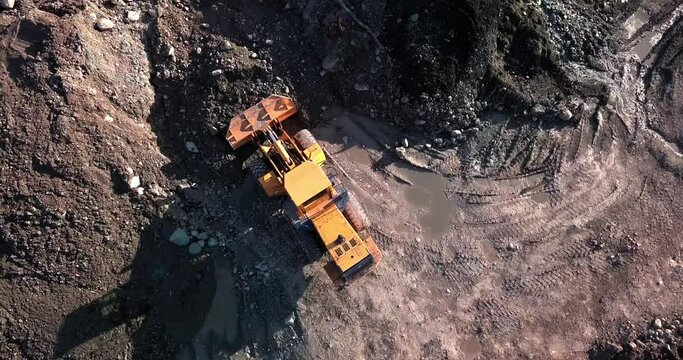 Large powerful yellow placer mining wheel operating yellow loader in Yukon brown dirt ground, Canada, directly above aerial