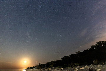 Fototapeta na wymiar night starry sky with rising moon over sea beach