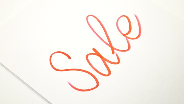 Man writes the word "Sale" in red marker on a white sheet of paper, preparing for the presentation