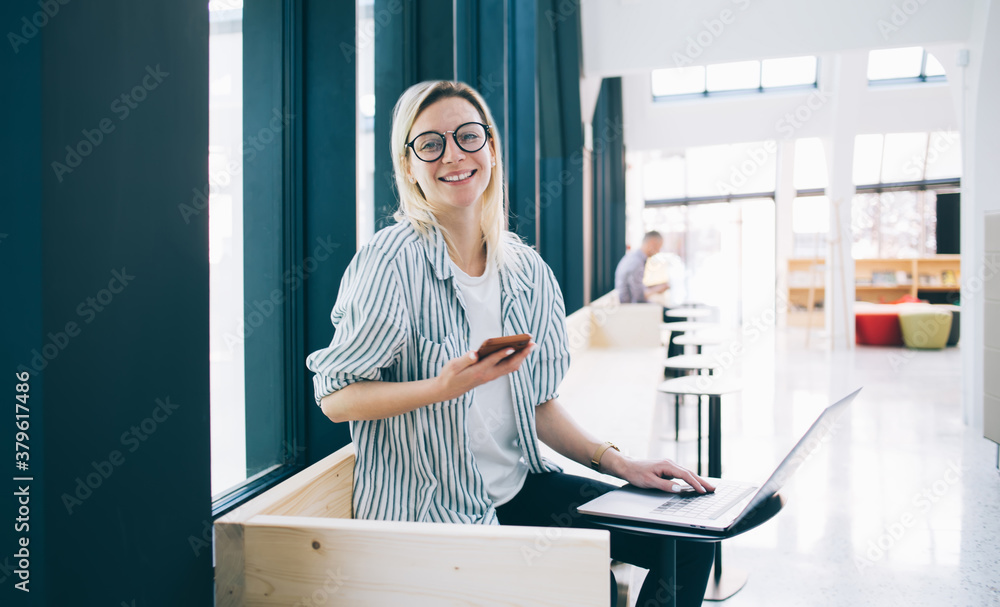 Poster portrait of cheerful female freelancer in stylish eyewear smiling at camera during mobility networki