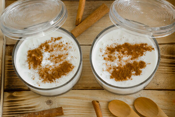 Traditional Turkish Rice Pudding in stylish glass bowls on wooden tray with cinnamon sticks and wooden spoons