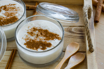 Traditional Turkish Rice Pudding in stylish glass bowls on wooden tray with cinnamon sticks and wooden spoons