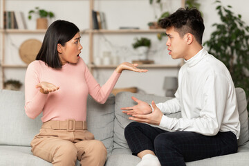 Asian Spouses Having Quarrel Sitting On Sofa At Home
