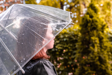 Autumn. Lonely sad woman under a transparent umbrella with rain drops walking in a park, garden. Rainy day landscape. Vintage Toned