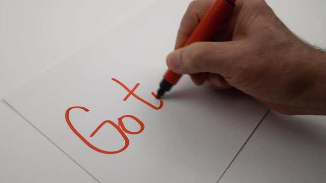 Man writes the phrase "Go to the goal!" in red marker on a white sheet of paper, preparing for the presentation