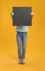 Woman holding black blank poster on yellow background. Mockup for design