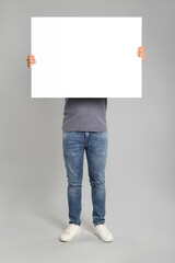 Man holding white blank poster on grey background. Mockup for design