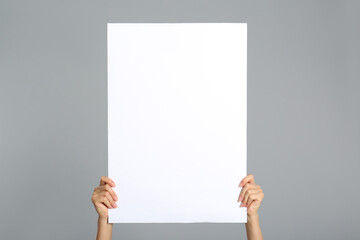 Woman holding white blank poster on grey background, closeup. Mockup for design