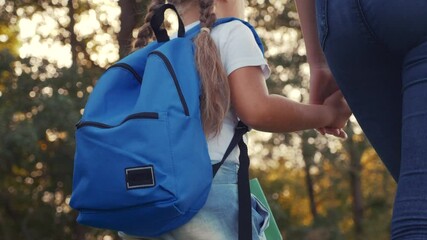 mom and daughter go to school. happy family education concept. schoolgirl with mom and daughter go hand in hand to school on footpath in lifestyle the park. little girl with a briefcase time to study - Powered by Adobe