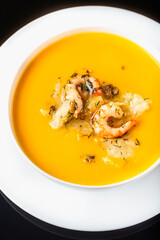 Diet pumpkin soup with shrimp, crouton, turmeric and greens. Healthy food. Black background.