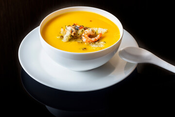 Diet pumpkin soup with shrimp, crouton, turmeric and greens. Healthy food. Black background.