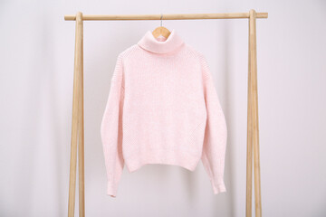 Stylish knitted sweater hanging on clothing rack near light wall