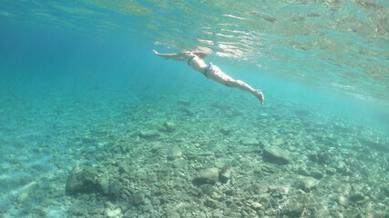 Underwater photo of unidentified woman swimming in beautiful pebble beach of Krovoulia near picturesque village of Frikes, Ithaki island, Ionian, Greece