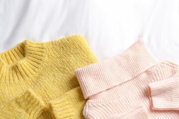 Stylish knitted sweaters on white fabric, flat lay