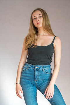 Portrait of a cute teenage girl wearing a black tank top and denim jeans posing looking at the camera on a grey background