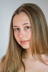 Naklejka premium Close up portrait of a pretty teenage girl with long natural blonde hair and smooth skin looking at the camera. Studio shot