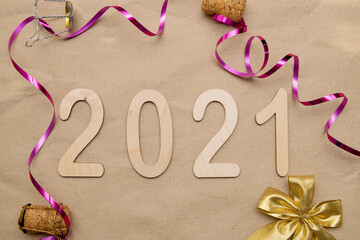 Light wooden numbers 2021 lie in the center on craft paper with packing tape, champagne corks, gold bow