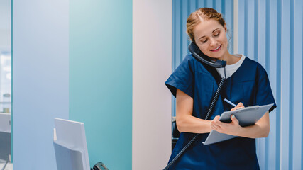 Caucasian female practitioner working at reception desk while answering phone calls and scheduling...