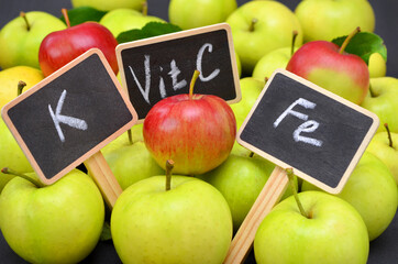 colorful red and green apples and tablets with the written words denoting the beneficial elements vitamin C potassium and iron 