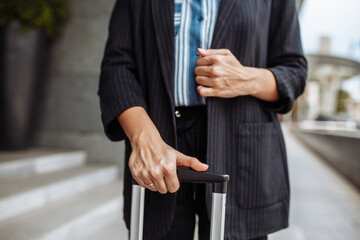 Close up of a professional business woman standing near the hotel's doors with a suitcase waiting for a taxi. Business trip and official look. Work and travel concept.