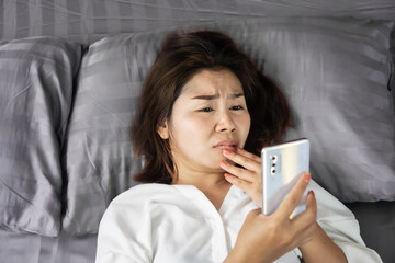 Fototapeta premium Asian woman hand holding smart phone in bed watching series tv late at night, social addiction concept 