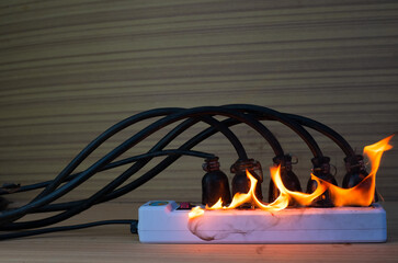 On fire multi socket with the connected power strip with a bunch of plugs on wood background © Thicha
