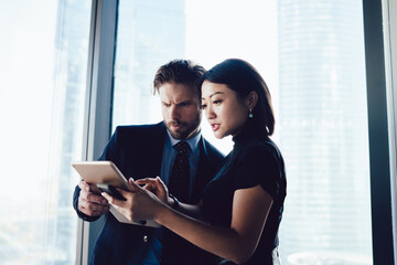 Obraz premium Diverse male and female partners checking mail on touch pad during working time in company office, multicultural entrepreneurs using technology for online banking operation connected to 4g wireless