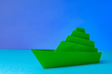 Paper boat on a blue background. Green multi-storey ship. Concept - loneliness. Lone ship close-up....
