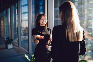 Smiling Asian businesswoman talking to female colleague in office corridor