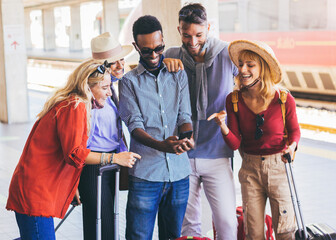 Multiracial group of friends wearing face mask using smartphone at train railway station. Young people booking online service transportation.