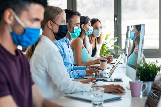 Successful concentrated business team wearing a hygienic facial mask while working together in the office keeping safe distances on coworking place.