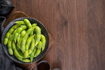 Fresh cooked boiled edamame in a plate on wooden tray and table background, healthy protein food concept.