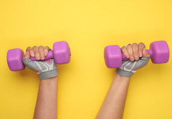 female hand in a pink sports glove holds a purple one kilogram dumbbell