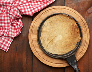 baked round big pancake in a black frying pan on a brown wooden table