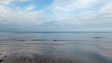 In the seascape there is a smooth sea surface under the beautiful evening sky of early autumn, a small wave rolls over the sandy shore, relaxation ...
