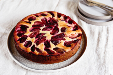 Homemade Ricotta Plum Cake on beige linen tablecloth. Cottage cheese casserole with vanilla, semolina and plums. Selective focus