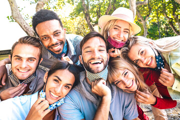 Multiracial friends taking happy selfie with open face masks after lockdown reopening - New normal friendship concept with young people having fun together out at public park - Bright vivid filter