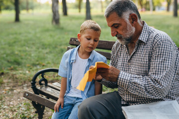 boy with his grandfather playing with paper airplane in city park